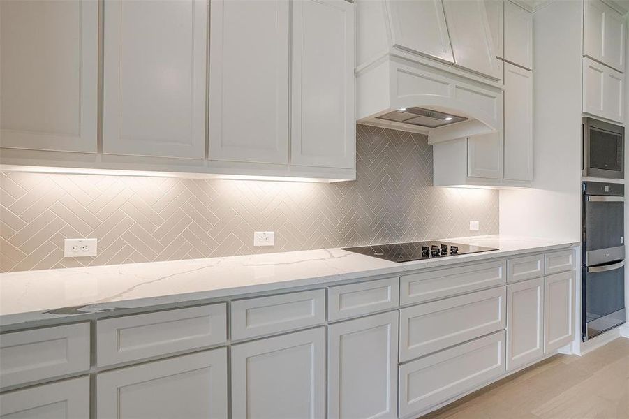 Kitchen featuring light hardwood / wood-style flooring, tasteful backsplash, white cabinets, appliances with stainless steel finishes, and light stone counters