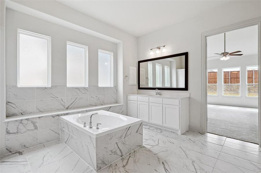 Bathroom featuring vanity, plenty of natural light, light marble finish floors, and a bath