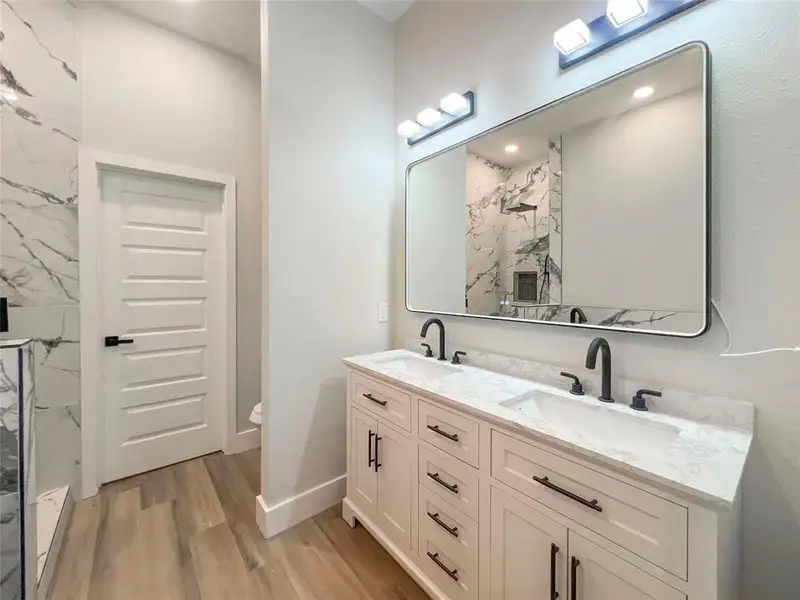 Full bathroom featuring wood finished floors, a sink, a marble finish shower, and double vanity Full bathroom featuring wood finished floors, a sink, a marble finish shower, and double vanity