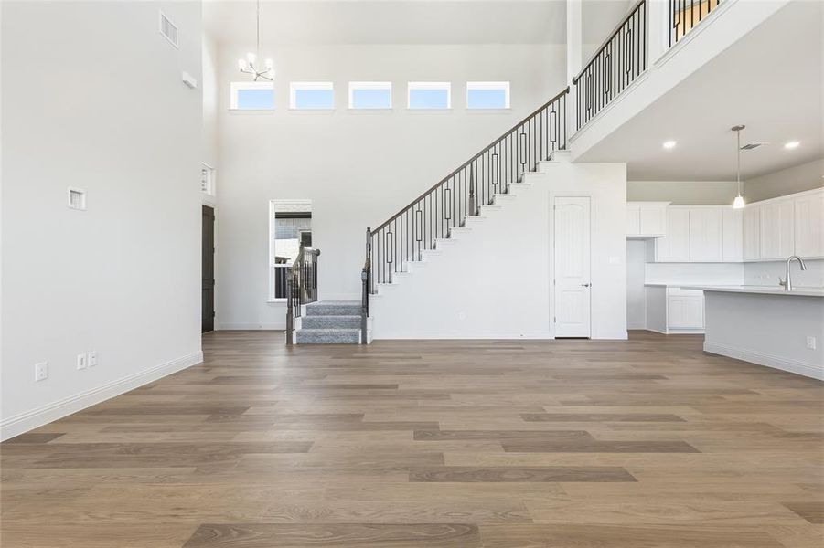 Unfurnished living room featuring light wood-style flooring, a high ceiling, and a chandelier