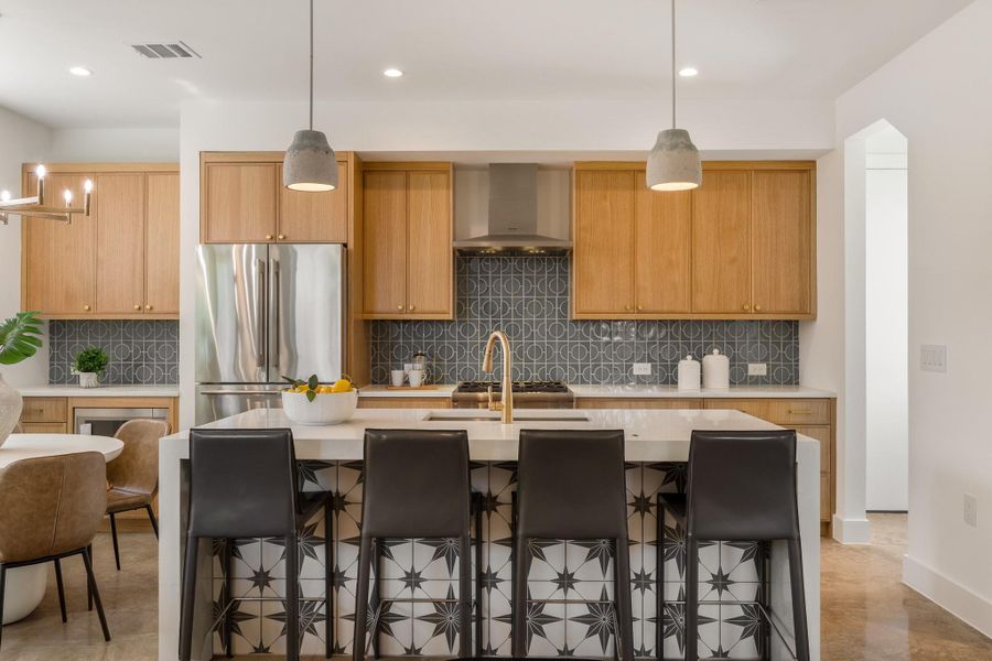 Warm wood cabinetry, striking tile work, quartz countertops, brass accents, and an oversized island make this kitchen a true centerpiece of the home.