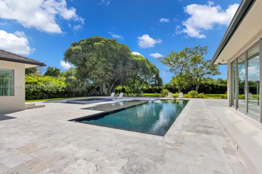 Outdoor living area featuring stone paver decking, an in-ground infinity-edge pool, a raised spa, and floor-to-ceiling glass sliding doors