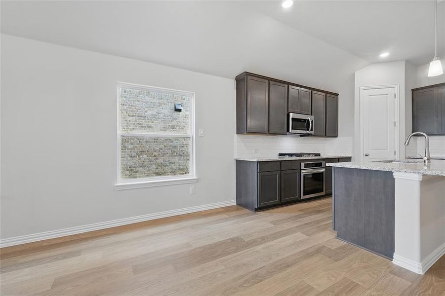 Kitchen featuring appliances with stainless steel finishes, a sink, light wood-style floors, tasteful backsplash, and light stone counters Kitchen featuring appliances with stainless steel finishes, a sink, light wood-style floors, tasteful backsplash, and light stone counters