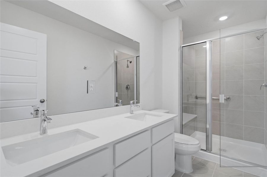 This move-in ready primary bathroom offers a spacious walk-in shower with built-in seat and tile surround, stained cabinetry topped with lite countertops, dual sinks, high ceilings, neutral paint, a large mirror, and sleek, modern finishes for a polished look.