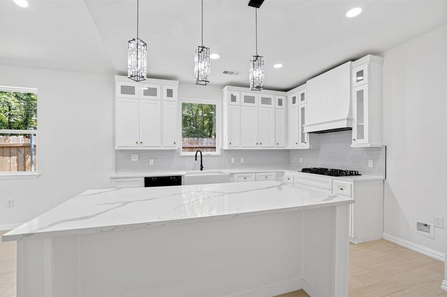 Spacious kitchen featuring a large island with a patterned countertop, white cabinetry with gold-tone hardware, a gas cooktop, and three pendant light fixtures