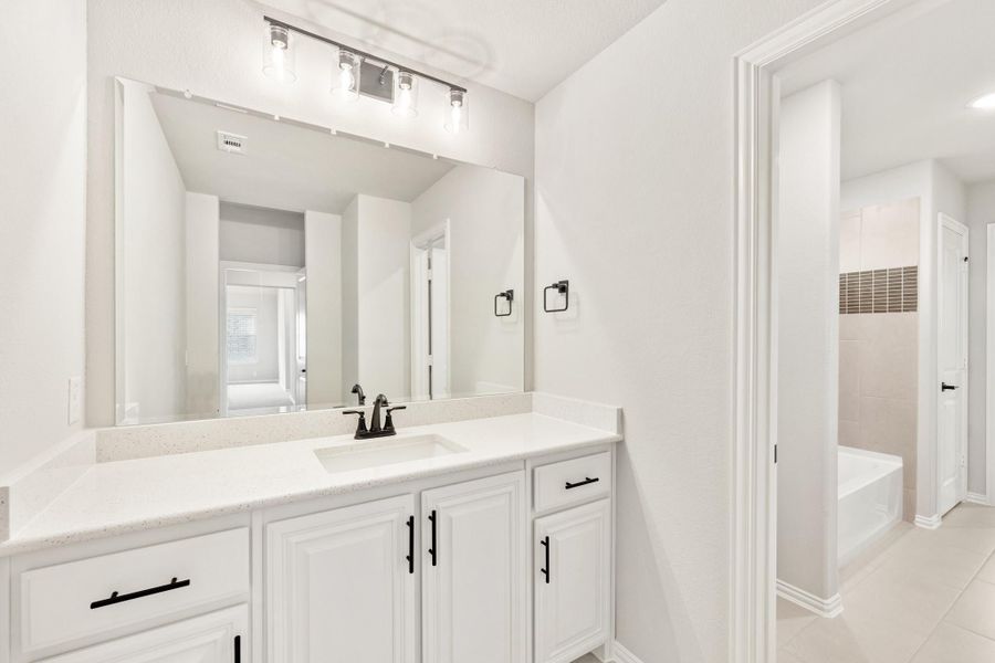 Bathroom with white vanity, quartz countertop, large mirror, and soaking tub visible in background