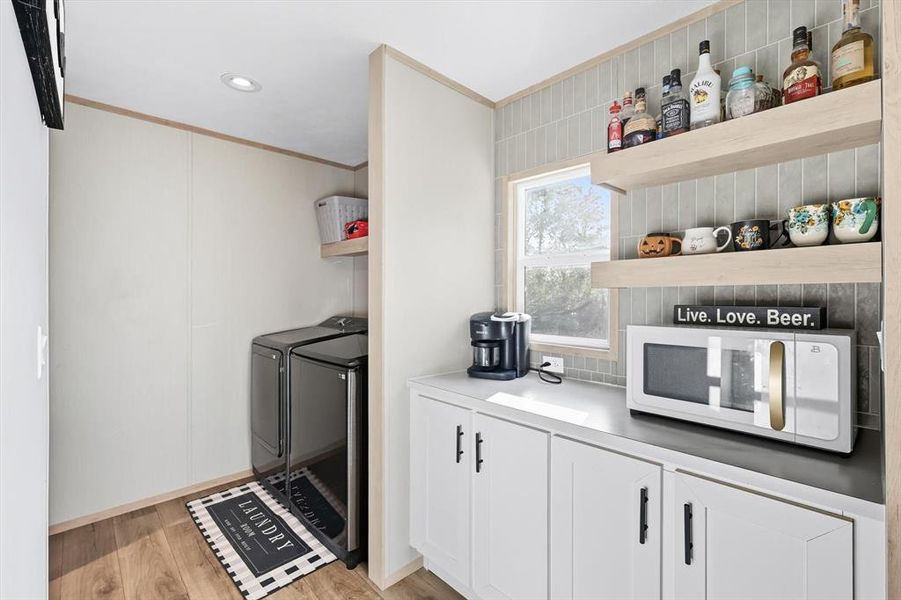 Kitchen with open shelves, white microwave, white cabinets, light wood-type flooring, and crown molding Kitchen with open shelves, white microwave, white cabinets, light wood-type flooring, and crown molding
