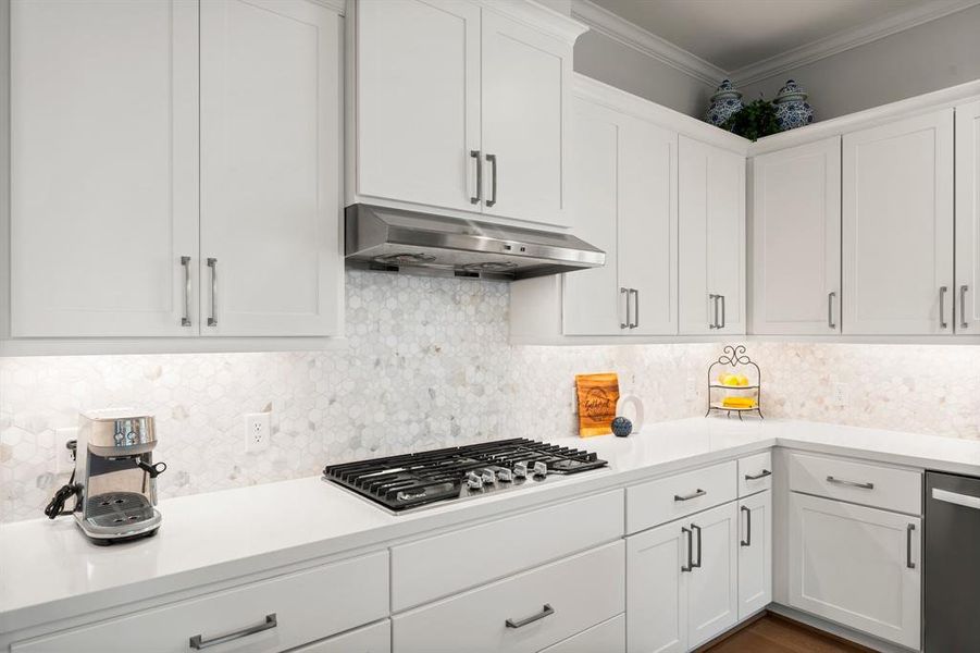 Kitchen boasts a stylish vent hood, gas stove, and mosaic backsplash tiling.