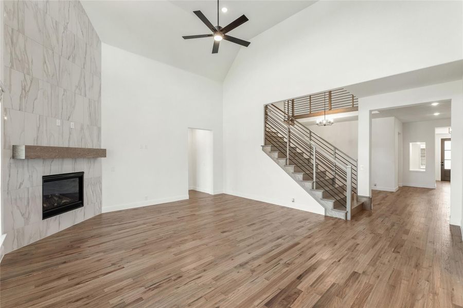 Open living room with vaulted ceiling, marble tile fireplace, hardwood floors, and modern staircase with metal railing