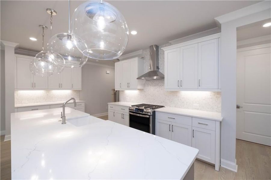 Kitchen featuring wall chimney range hood, sink, stainless steel gas range, light stone countertops, and white cabinets