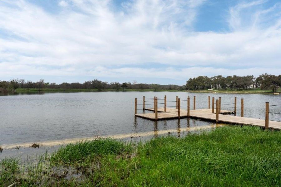 Expansive body of water with a wood dock featuring rope railings, surrounded by lush green grass and mature trees