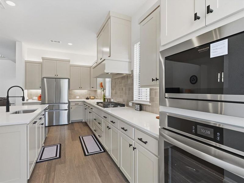 Kitchen featuring wood-finish flooring, light-toned cabinetry with dark hardware, stainless steel appliances, and solid surface countertops