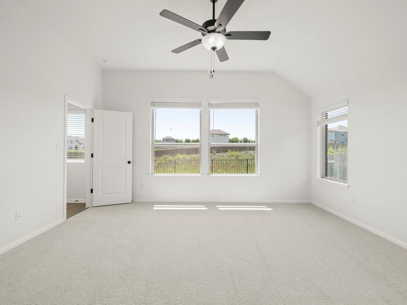 Spacious room featuring vaulted ceilings, a ceiling fan with integrated lighting, and multiple windows providing ambient light