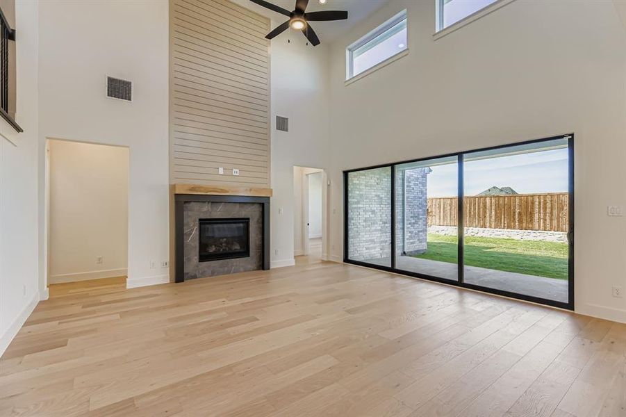 Unfurnished living room with light wood-style flooring, a tiled fireplace, a high ceiling, and a ceiling fan