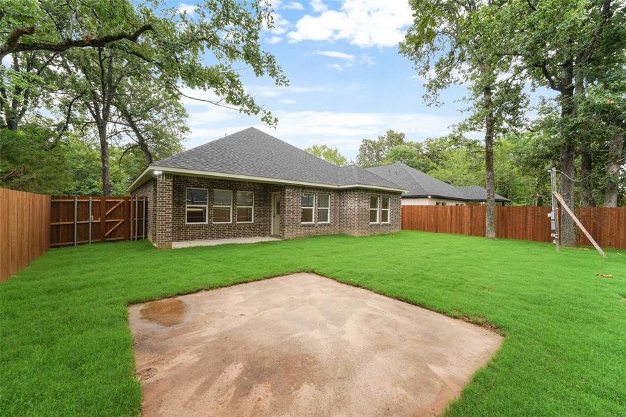 Expansive fenced backyard featuring a concrete patio, lush green lawn, mature trees, and a brick exterior Expansive fenced backyard featuring a concrete patio, lush green lawn, mature trees, and a brick exterior