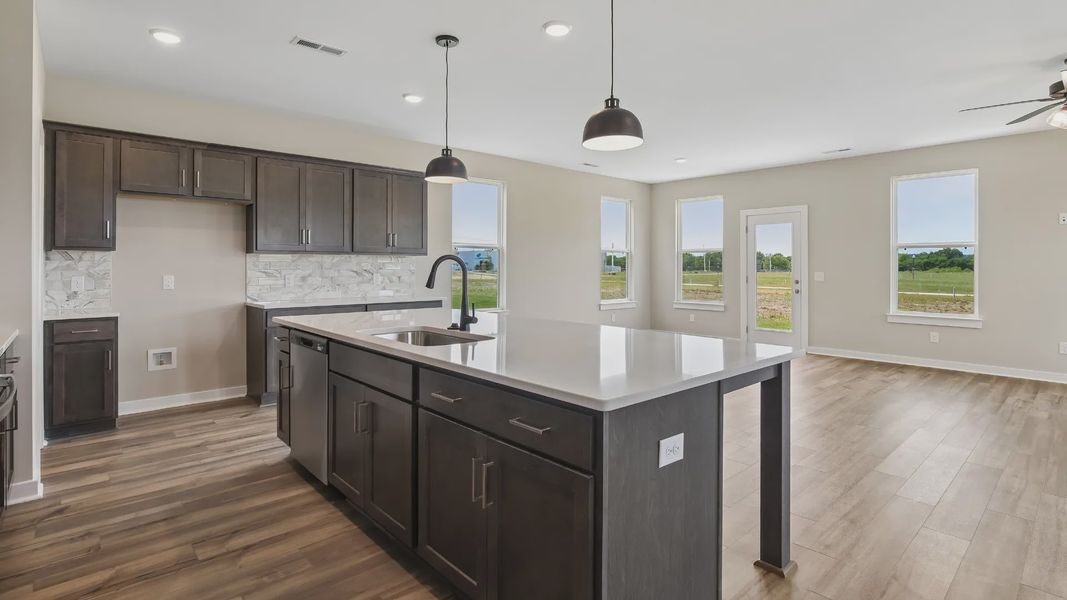 Kitchen with dark cabinetry, quartz countertops, pendant lighting, and tile backsplash Kitchen with dark cabinetry, quartz countertops, pendant lighting, and tile backsplash