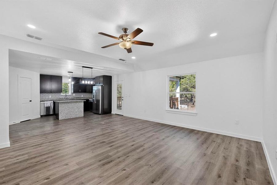 Unfurnished living room featuring healthy amount of natural light, dark wood finished floors, ceiling fan, a textured ceiling, and recessed lighting