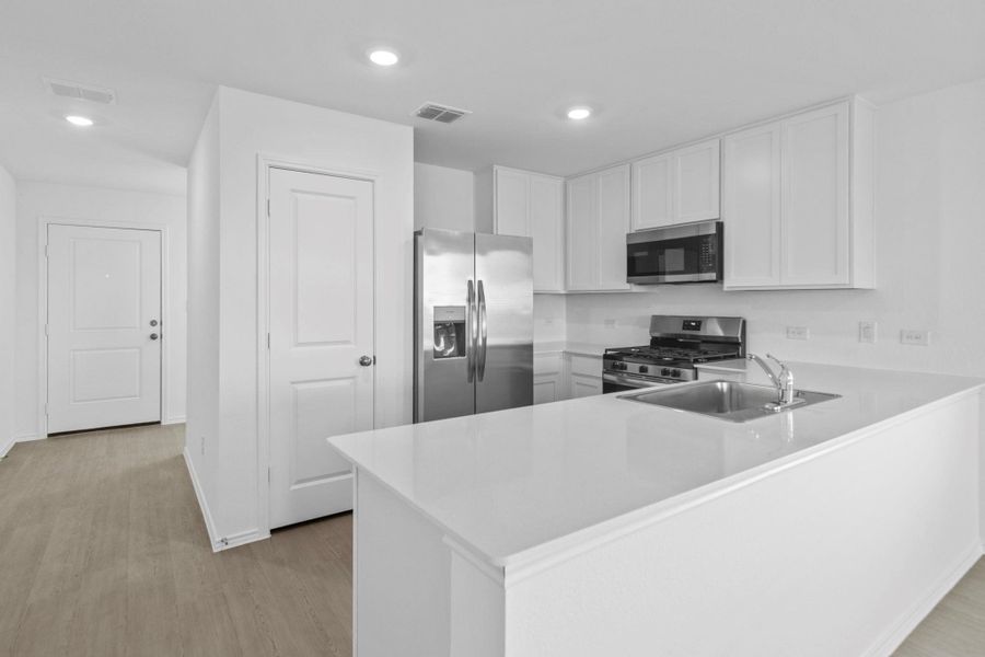 Kitchen with a peninsula, stainless steel appliances, white cabinetry, light wood finished floors, and recessed lighting