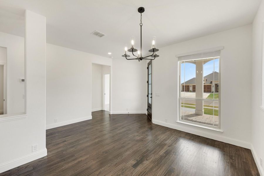 Empty dining room with dark hardwood floors, white walls, black chandelier, and large window