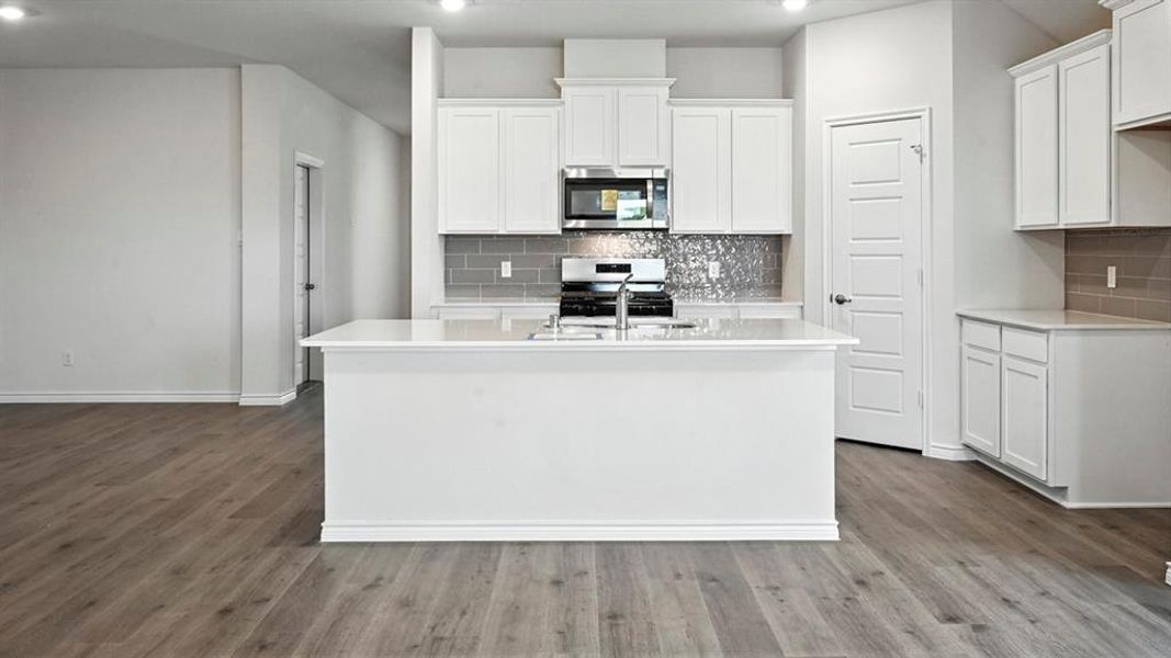 Modern kitchen featuring a central island with an integrated sink, white cabinetry, quartz-finish countertops, wood-finish flooring, and recessed lighting Modern kitchen featuring a central island with an integrated sink, white cabinetry, quartz-finish countertops, wood-finish flooring, and recessed lighting