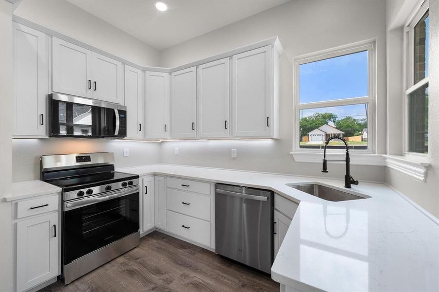 Modern kitchen featuring white shaker cabinetry, stainless steel appliances, light-toned countertops, and wood-finish flooring