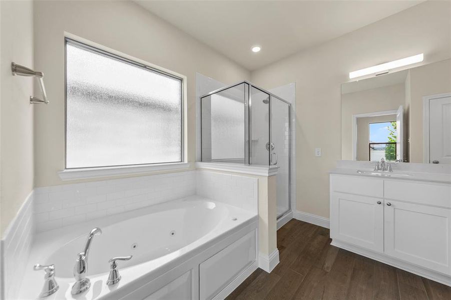 Bathroom featuring a soaking tub with polished chrome fixtures, a separate glass-enclosed shower, wood-finish flooring, a white vanity with an integrated sink, and an expansive mirror