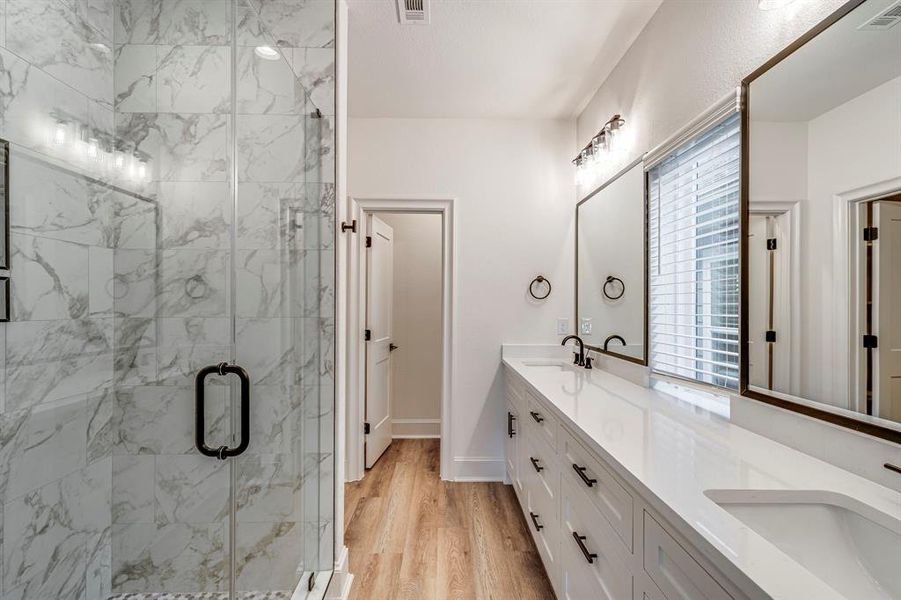 Full bathroom with a sink, a marble finish shower, visible vents, and wood finished floors Full bathroom with a sink, a marble finish shower, visible vents, and wood finished floors