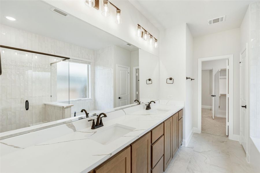 Master bathroom with double sinks, quartz countertop, wood vanity, glass shower, and walk-in closet entrance