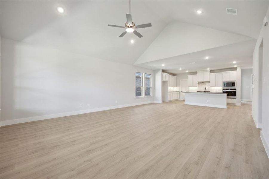 Unfurnished living room featuring ceiling fan, high vaulted ceiling, and light wood-type flooring