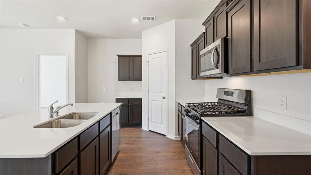 Kitchen with appliances with stainless steel finishes, a center island with sink, dark wood-style flooring, light stone counters, and recessed lighting Kitchen with appliances with stainless steel finishes, a center island with sink, dark wood-style flooring, light stone counters, and recessed lighting