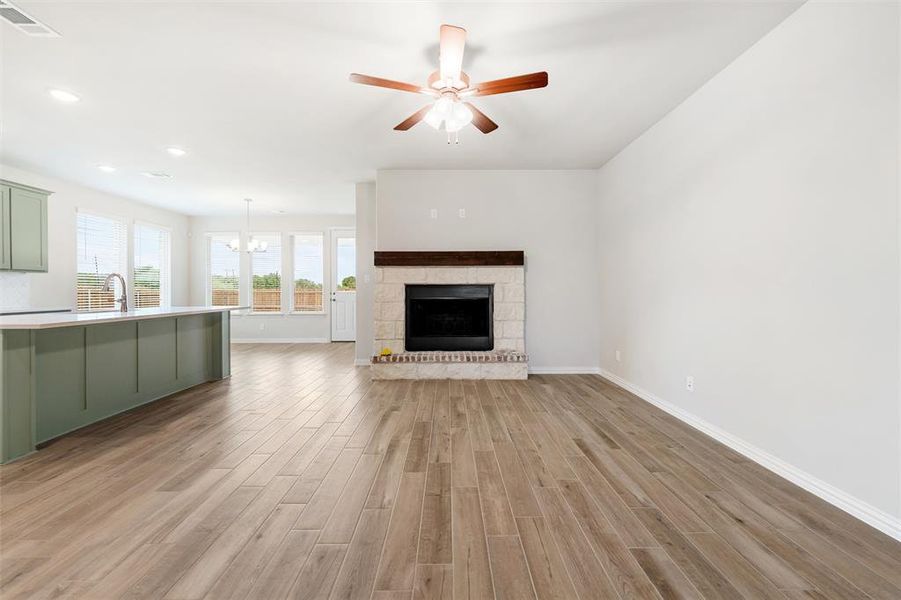 Unfurnished living room featuring ceiling fan, a stone fireplace, light wood finished floors, recessed lighting, and a chandelier Unfurnished living room featuring ceiling fan, a stone fireplace, light wood finished floors, recessed lighting, and a chandelier