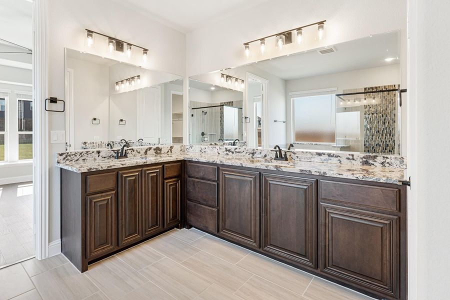 Master bathroom with L-shaped double vanity, dark wood cabinets, granite countertops, and large mirrors with overhead lighting. Master bathroom with L-shaped double vanity, dark wood cabinets, granite countertops, and large mirrors with overhead lighting.