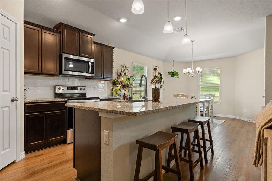 Kitchen featuring dark brown cabinets, stainless steel appliances, tasteful backsplash, a kitchen breakfast bar, and light stone countertops
