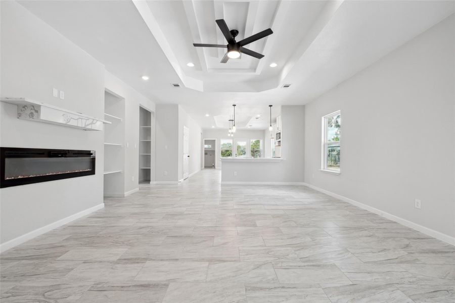 Unfurnished living room with built in shelves, a tray ceiling, ceiling fan, a glass covered fireplace, and recessed lighting Unfurnished living room with built in shelves, a tray ceiling, ceiling fan, a glass covered fireplace, and recessed lighting