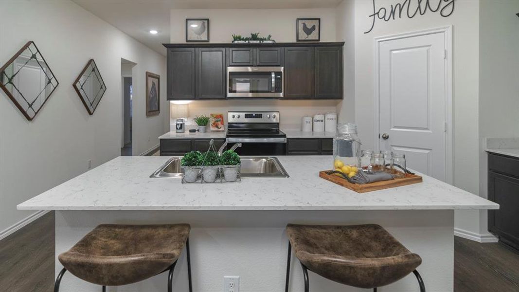 Kitchen with dark wood-style floors, stainless steel appliances, a kitchen bar, and a kitchen island with sink