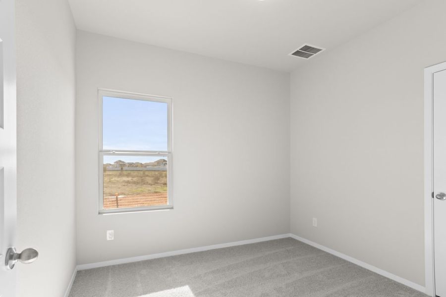 Image of a bedroom with tan carpeting, light grey walls and a window