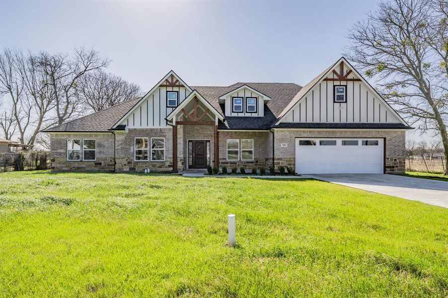 View of front of home featuring brick siding, a shingled roof, board and batten siding, driveway, and a front lawn