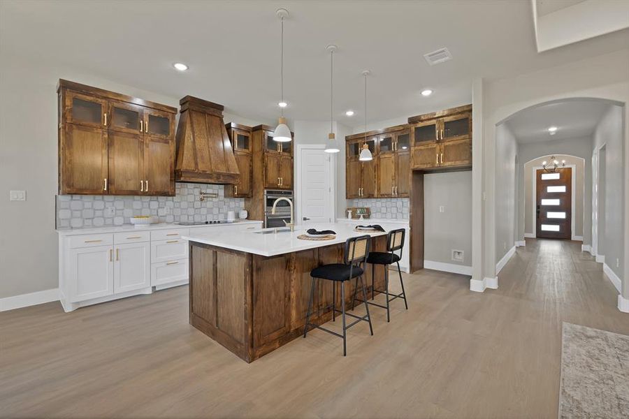 Kitchen featuring premium range hood, arched walkways, baseboards, light wood finished floors, and recessed lighting