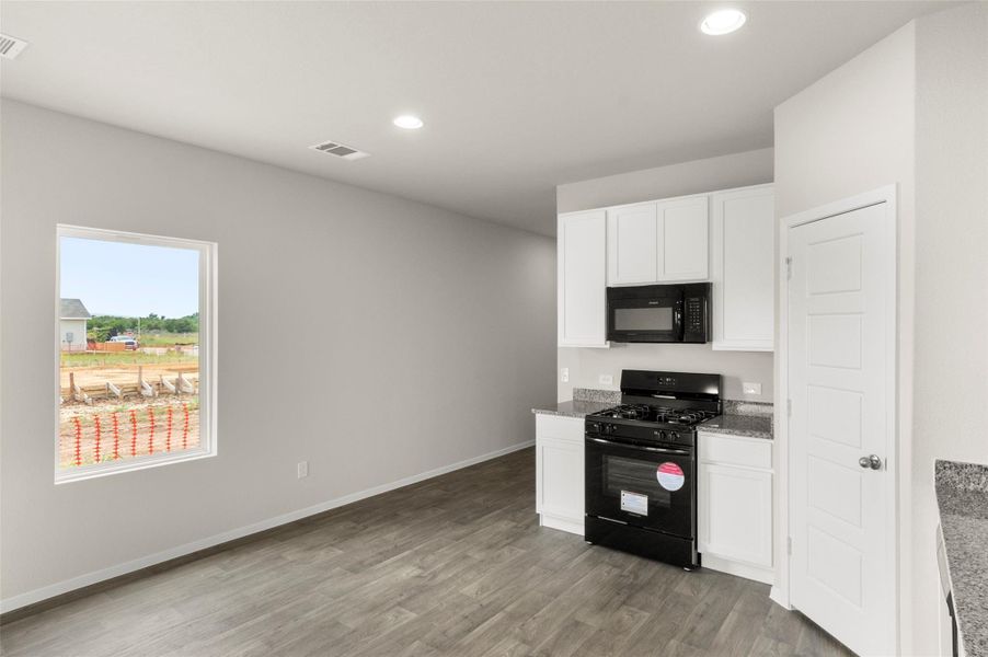 Kitchen featuring black appliances, white cabinetry, light stone countertops, light wood-style floors, and recessed lighting