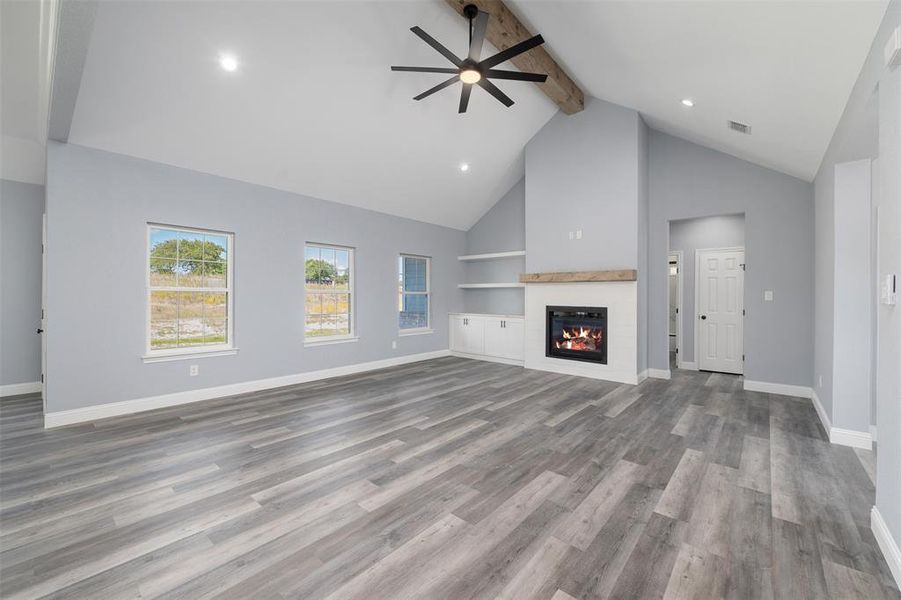 Unfurnished living room with beamed ceiling, high vaulted ceiling, a glass covered fireplace, dark wood finished floors, and ceiling fan Unfurnished living room with beamed ceiling, high vaulted ceiling, a glass covered fireplace, dark wood finished floors, and ceiling fan