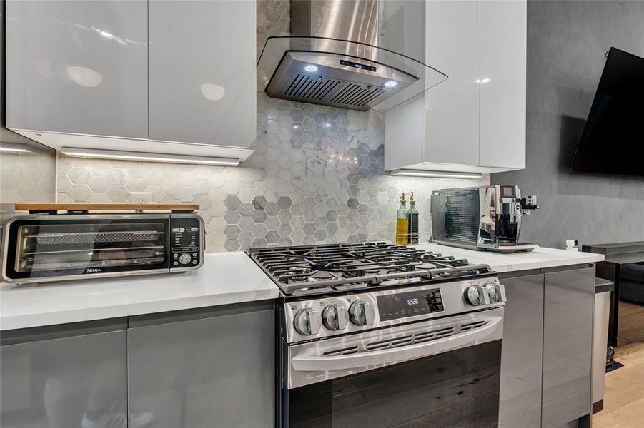 Kitchen with gas range, range hood, tasteful backsplash, modern cabinets, and white cabinets Kitchen with gas range, range hood, tasteful backsplash, modern cabinets, and white cabinets