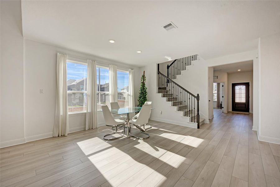 Bright open-concept space featuring wood-finish flooring, a contemporary staircase with iron balusters, three large windows, recessed lighting, and a paneled entry door with leaded glass accents