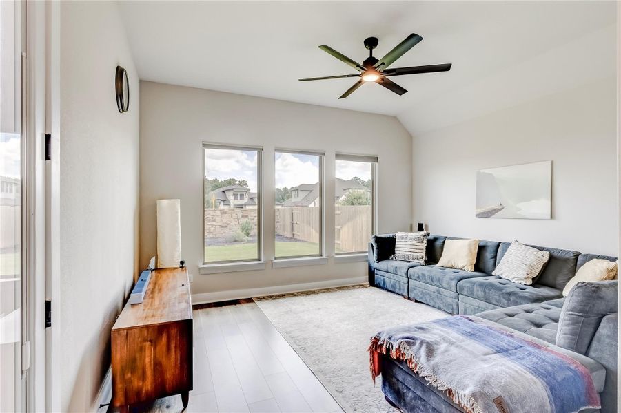 A luminous Gameroom features high ceilings, hardwood flooring, and expansive windows overlooking a verdant private yard.