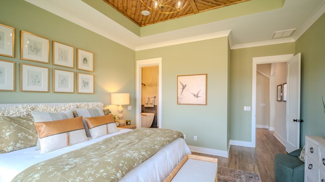 Spacious primary suite with tray ceiling, hard surface flooring, and access to primary bathroom Spacious primary suite with tray ceiling, hard surface flooring, and access to primary bathroom