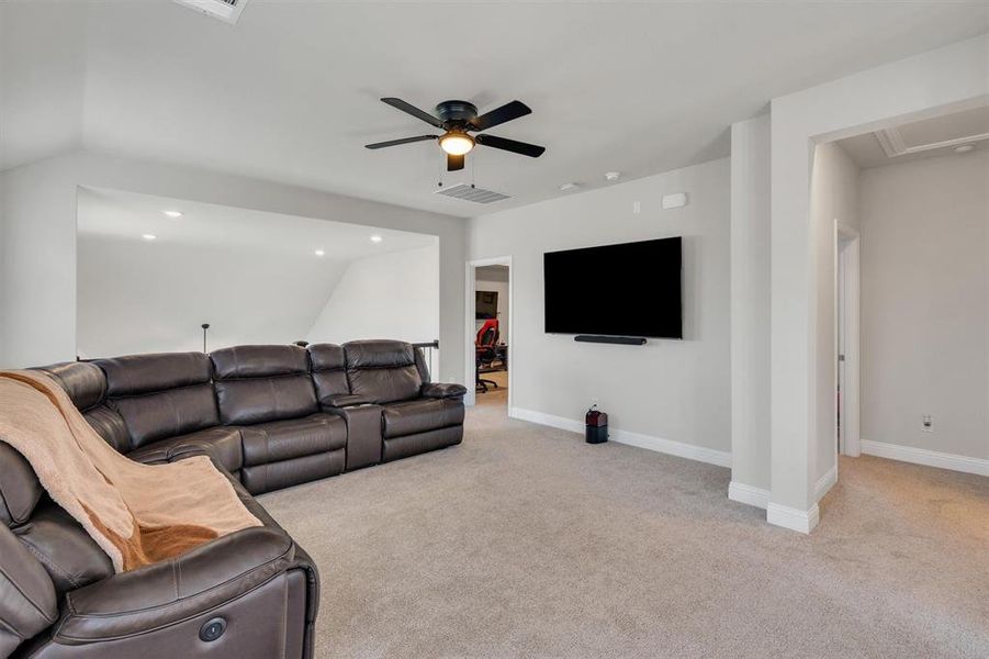 Spacious carpeted room featuring a ceiling fan with integrated lighting, wall-mounted television, and recessed ceiling lights