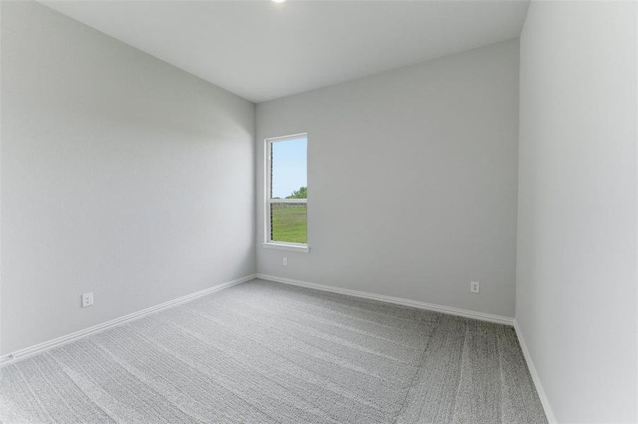 This room features light grey walls, light grey patterned carpeting, white baseboards, and a window providing natural light and a view of green space