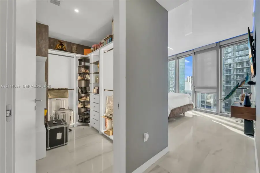 Walk-in closet featuring custom white built-in shelving, a rotating shoe rack, and stone-finish tile flooring throughout Walk-in closet featuring custom white built-in shelving, a rotating shoe rack, and stone-finish tile flooring throughout