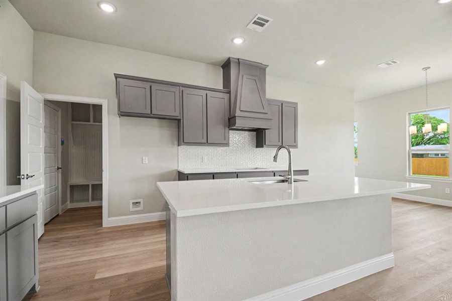 Modern kitchen featuring a large center island with a white countertop, gray cabinetry, a decorative range hood, and a white mosaic tile backsplash Modern kitchen featuring a large center island with a white countertop, gray cabinetry, a decorative range hood, and a white mosaic tile backsplash
