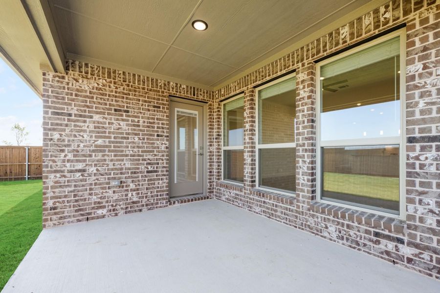 Covered back patio with brick exterior, back door, and large windows overlooking fenced yard