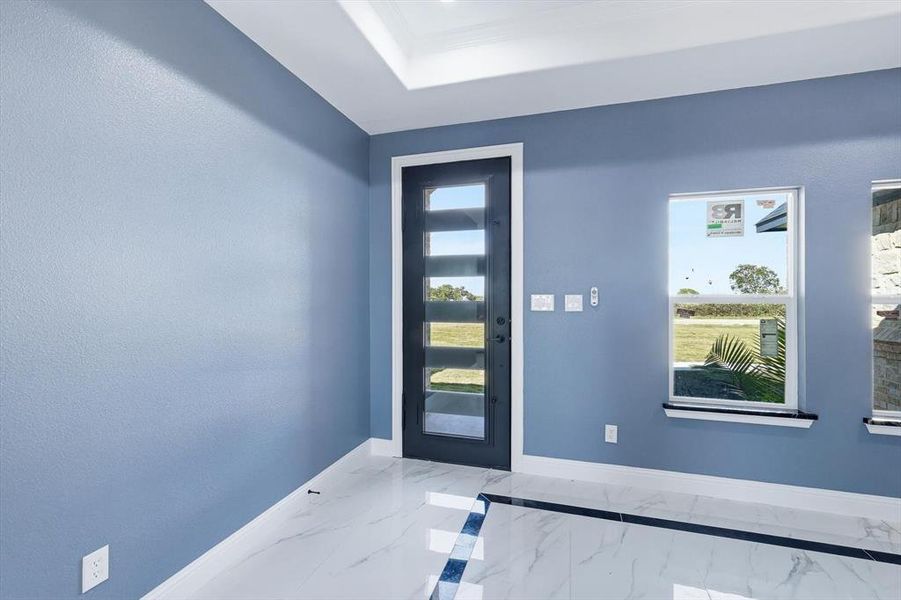 Entryway with marble finish floors, a raised ceiling, and ornamental molding